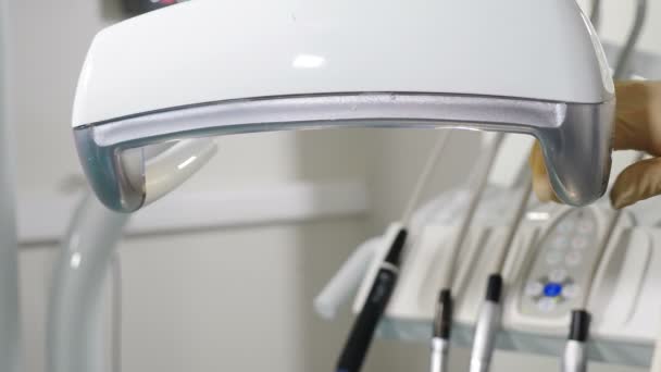 La mano femenina que ajusta la iluminación dental del led antes de la operación, herramientas del dentista y equipo dental profesional que consigue listo para ser utilizado por el ortodoncista. Estomatóloga hembra ajustando operatorio dental — Vídeos de Stock