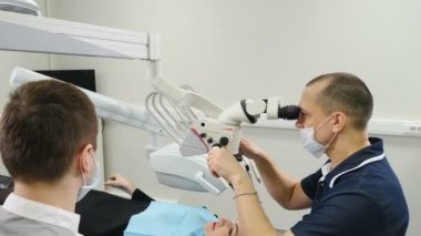 Mikroskop kullanan doktor. Modern diş kliniğinde hastayı tedavi eden diş hekimi. Ortodontist bir asistanla çalışıyor. Operasyon özel Diş İçi Kontrol Dijital Mikro Kamera kullanılarak gerçekleştirilir