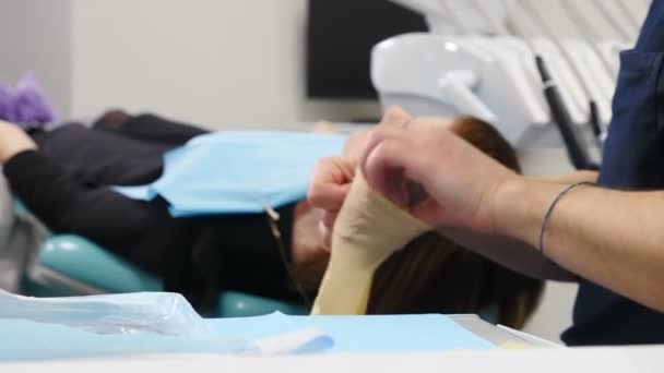 Nahaufnahme eines zugeschnittenen Rahmens eines männlichen Zahnarztes in medizinischem Gewand, der in der Zahnarztpraxis einen medizinischen Handschuh am Arm trägt und sich darauf vorbereitet, den Patienten zu nehmen. 4k — Stockvideo