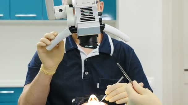 Doctor usando microscopio. Dentista atendiendo a paciente en clínica dental moderna. Ortodoncista trabaja con un asistente. La operación se lleva a cabo utilizando una microcámara digital especial de control intraoral dental — Vídeos de Stock