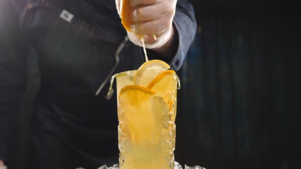 Acérquese chef de mano exprimiendo naranja en cóctel de frutas frescas en cámara lenta. jugo goteando de fruta. Cocinar en la cocina. Fondo negro. hd — Vídeos de Stock