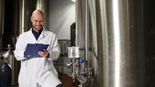 Concetto di produzione della birra. Attento addetto alla manutenzione che scrive negli appunti del birrificio. Il dipendente del birrificio controlla l'attrezzatura. Lavoratore di birreria in camice da laboratorio a controllare le attrezzature per bevande — Video Stock