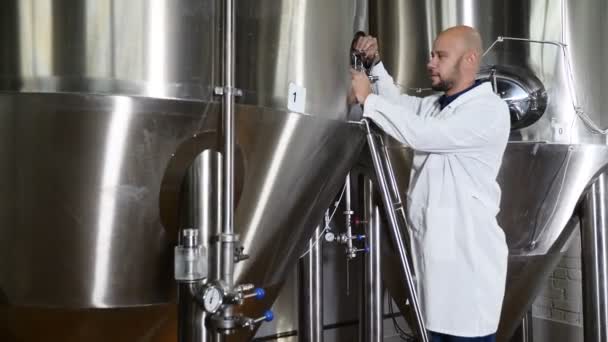 Concepto cervecero. Trabajador de mantenimiento atento escribiendo en portapapeles en la cervecería. El empleado de la cervecería comprueba el equipo. Trabajadora cervecera en bata de laboratorio revisando equipos de bebidas en fábrica. 4k — Vídeo de stock