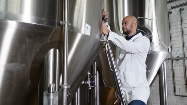 Concepto de producción de cerveza. Trabajador de mantenimiento atento escribiendo en portapapeles en la cervecería. El empleado de la cervecería comprueba el equipo. Trabajador cervecero en equipo de verificación de bata de laboratorio en — Vídeo de stock