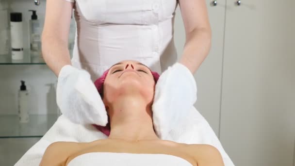 Beauty clinic. Young woman gets professional facial procedure. Beautician warms out facial mask off female client with a towel. hd — Stock Video