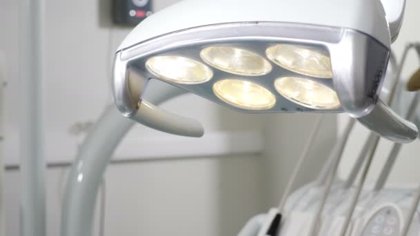 Dicht panoramisch uitzicht van tandheelkundige lamp in de tandheelkundige orthondist kamer. Een tandarts schakelt aan en past het licht aan voor een snelle tanden controle. voorbereiding voor chirurgie. 4k — Stockvideo
