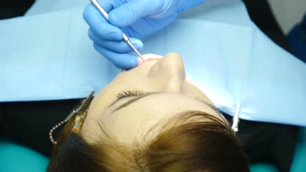 Bir kontrol ve diş temizliği için diş hekimi ofisinde bir kadın hastanın portresikadar kapatın. Dişçi genç bir kadının dişlerini aynayla kontrol ediyor. Diş hekimi dişleri dikkatle inceler. At — Stok video