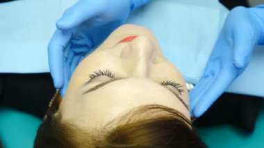 Diş hekimi dokunma çene eklemi ile muayene. Diş sandalyede genç kadının yakın çekim. Eldivenli tanınmayan doktor kadın hastayı kontrol ediyor. 4k