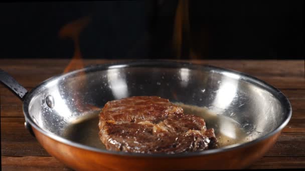 Images au ralenti de steak de bœuf frais avec des herbes sur une poêle enflammée. grand steak est frit dans une poêle avec des épices et une brindille de thym dans la cuisine du restaurant. Préparer un dîner gastronomique, en haute qualité — Video