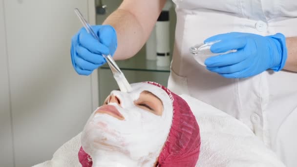 En el centro de belleza. Cosmetolodista femenina hace cuidado de la piel anti-envejecimiento máscara facial blanca. Macro. hd — Vídeo de stock