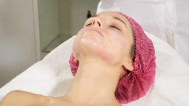 Mavi eldivenli güzellik uzmanı genç kadının yüzüne krem sokuyor. Yüz kurtarma ve gençleştirme kavramı. Dolabındaki kadın güzellik uzmanının yakını. Kozmetolojist müşterilerinin yüzüne maske uygular. Hd