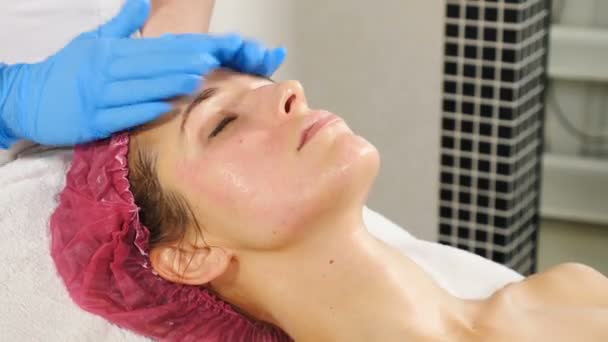 Kosmetolog massage kvinnlig klient. Beauty terapeut förbereder kvinna ansikte för behandling i salongen. Ung kvinna får ansiktsbehandling i skönhetssalongen. Hd — Stockvideo