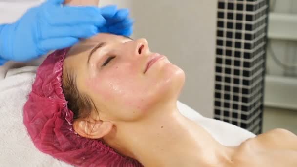 Kosmetolog massage kvinnlig klient. Beauty terapeut förbereder kvinna ansikte för behandling i salongen. Ung kvinna får ansiktsbehandling i skönhetssalongen. Hd — Stockvideo