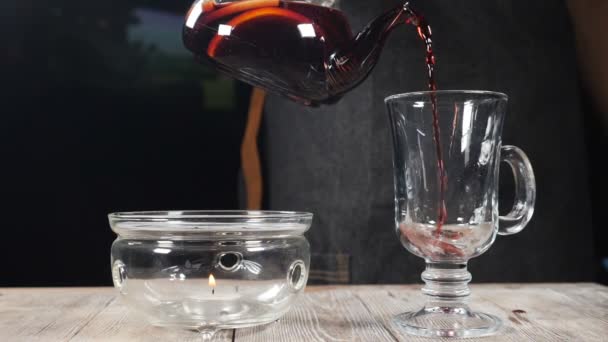 Barkeeper, der in einem gemütlichen Restaurant heißen Früchtetee in ein leeres Glas auf schwarzem Hintergrund gießt. Zeitlupe. heißes gesundes Getränk in Glasteekanne. hd — Stockvideo