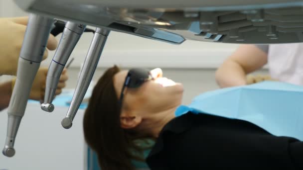 Procedimiento dental borroso en la clínica moderna. El equipo dental en primer plano está en foco. Odontólogo masculino examinando paciente. Médico manos. Paciente femenina con gafas de sol puestas. 4k — Vídeos de Stock