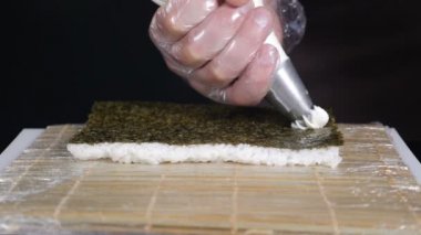 Yavaş hareket gıda video. Pasta torbası ile Nori üzerinde krem peynir dökme. Şef aşçı rulo, Sushi rulo yapma süreci. Ellerinizi kapatın. Hd