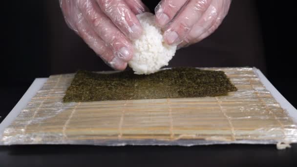 Potravní video. Mistr sushi šíří rýži na nori. Zpomaleně. Sushi kuchař připravuje rýži pro sushi roll na černém. Míč na vzestupu. Hd — Stock video