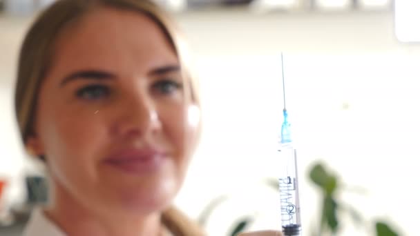 Porträtt av en suddig glad leende kvinnlig kosmetolog i skönhetsklinik förbereder spruta för injektion titta rakt på kameran. Närbild fokuserad spruta. Begreppet proffs. Skönhetskoncept — Stockvideo