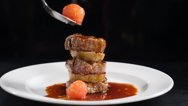 Slow Motion Food video concept. rundvlees medaillon prachtig zet een op een ander gegoten met heerlijke saus op witte plaat. Chef zet een gepekelde tomaat bovenop. Spatten in slow mo. HD — Stockvideo