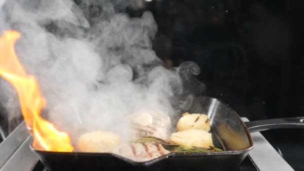 Vídeo de comida en cámara lenta. Los chefs cocinan platos flamencos a la parrilla en la cocina del restaurante. De cerca. Carne y patata en la sartén encendida. Concepto de cocina, chef, gourmet, comida italiana. hd — Vídeo de stock