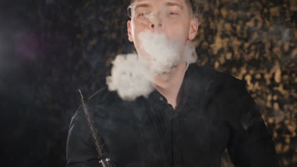 Un joven guapo fumando narguile. chico caucásico fumar tabaco con sabor. Apague el humo de cerca sobre fondo oscuro. forma redonda de vapor está volando en el aire. Niebla mágica del arte, mal concepto de habbit. despacio — Vídeo de stock