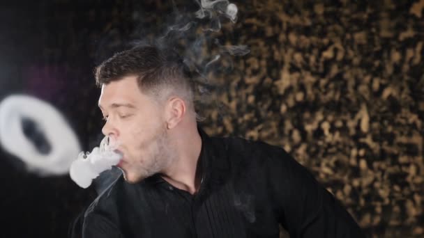 Retrato del guapo joven caucásico fumando narguile y haciendo anillos de humo en el cuarto oscuro. Niebla mágica del arte, malos hábitos. Hombre brutal relajándose en el bar de narguile. En cámara lenta. hd — Vídeos de Stock