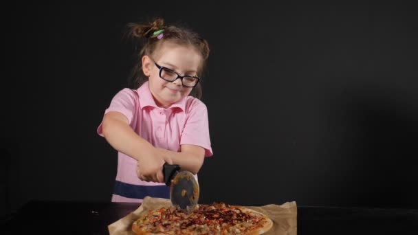 Bastante pequeña chica caucásica corte deliciosa pizza casera con cortador redondo. Aislado sobre fondo negro. Disparo en cámara lenta. hd — Vídeos de Stock