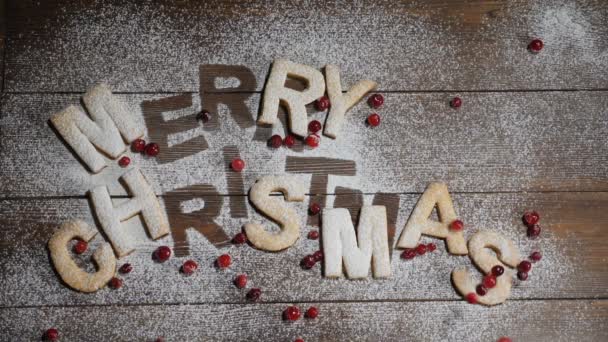 Feliz Año Nuevo y concepto de fiesta. .. Feliz Navidad nota escrita con galletas letras sobre tabla de madera marrón con polvo blanco como si la nieve. Se están tirando bayas rojas. en cámara lenta. hd — Vídeo de stock