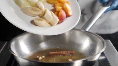 Restoran yavaş hareket gıda video. Aşçı dilimlenmiş meyve koyarak: muz, tava üzerinde kayısı. Dondurma ile flambe tarzı tatlı pişirme. Hd