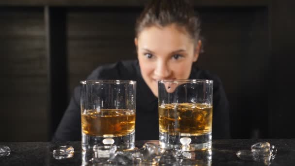 Retrato de uma empregada de bar sorridente feliz a olhar para a câmara através de copos de uísque atrás do balcão do bar. Os óculos estão concentrados. hd — Vídeo de Stock