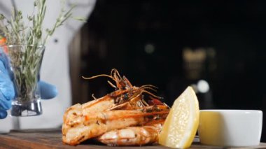 Son dokunuş konsepti. Restoran yemeği servisi. Eldiven şef kavrulmuş kaplan karides ve dilimlenmiş kireç ile gemide biberiye ve biberiye ile küçük bir vazo koyar. Yavaş çekim. Hd