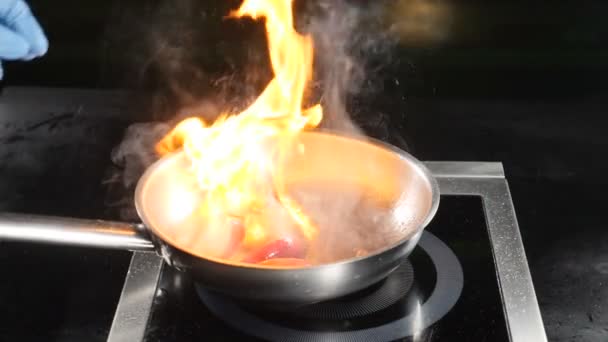 Conceito de vídeo alimentar. Chef em luvas azuis cozinhar prato flambe na cozinha do restaurante. Pêssego fatiado a ser posto em chamas. Fecha. hd — Vídeo de Stock