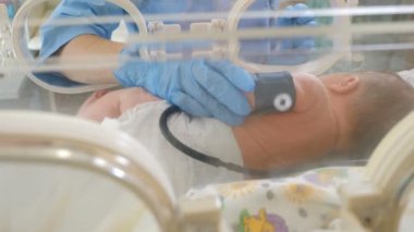 Doktor ellerinin bebek kuluçka makinesindeki bebeğe tıbbi sensörler ilerlerken çekilmiş yakın çekimi. yoğun tedavi doktoru prematüre bebeği kuvöze bağlar, yenidoğanın taşınmasıiçin hazırlanır. 4k