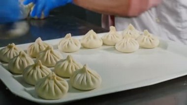Gıda video konsepti. Şef khinkali yapıyor. Ulusal Gürcü mutfağı. Yakından kapatın. Hazır köfteleri tepsiye koyuyor. 4k