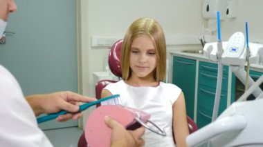 Sağlık sigortası konsepti. Diş hekimi, diş fırçasıyla nasıl diş temizleyeceğini çene modelinde gösteriyor. Ağız hijyeni. Diş hekimi, dişçi kliniğinde güzel bir kıza diş fırçalamayı öğretir. 4k