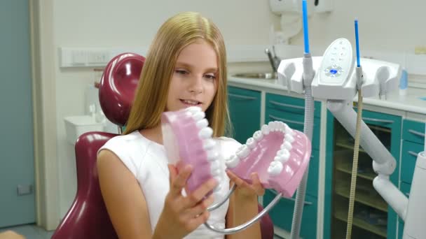 Odontología infantil. Concepto de protección dental. Linda niña de 10 años con modelo de dientes en las manos. Sonriente paciente alegre en el consultorio del dentista. Disparo en 4k — Vídeo de stock