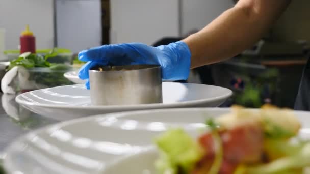 Detailní záběr kuchaře ruka zvedající kulinářský prsten při vaření salátu. Restaurace spěchá. Bílé talíře na stole. Shot in 4k