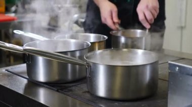 Restoran mutfak videosu. Büyük sobanın üstünde kaynamış tencereler. Çalışanlar acele ediyor. Sıcak sudan çıkan beyaz buhar. Şef çalışıyor. Yemek pişirme süreci. 4K 'da çekilmiş.