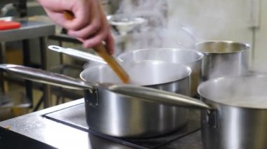 Lokanta mutfağında video çekimi. Kapatın. Kaynar suyla tencereleri karıştıran erkek el. Pişirme telaşı. Mutfak aletinden beyaz buhar çıkıyor. 4K 'da çekilmiş.
