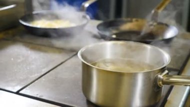 Restoranın mutfağında çekilmiş bir fotoğraf. Şef dikkatsiz bir şekilde deniz mahsullerini kızartma tavasına koyuyor. Kaynayan tencereden çıkan beyaz buharla vurulmuş. Meşgul restoran mutfağı. 4K 'da çekilmiş.