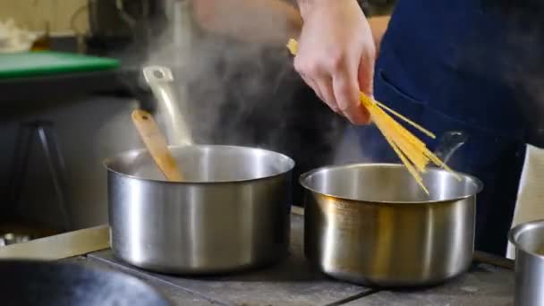 Upptaget restaurangkökskoncept. Team av kockar och kökspersonal tillagar och serverar mat i kommersiellt kök. Snabbt. Närbild. Lägger pasta i kokande vatten. Skjuten i 4k — Stockvideo