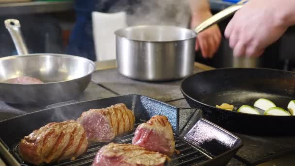 Restaurante rush na cozinha. Chef transforma bacon com pinças de metal na superfície quente da grelha. homem com pinças pega, torneiras vira carne. Tiros em 4K — Vídeo de Stock