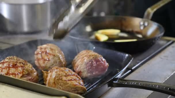 Jefe usando tong para encender la carne en la parrilla. .. Grill, sabroso bistec. De cerca. Restaurante prisa en la cocina. Chef gira tocino con pinzas de metal en la superficie caliente de la parrilla. hombre con pinzas recoge, golpecitos gira — Vídeo de stock