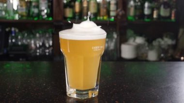 Buz küpleri bira dolu bardağa düşüyor. Ağır çekim. Bar tezgahında köpük ve su sıçraması. Beslenme ve içecek konsepti. Bardaktan dökülen biralar bitlenir. hd