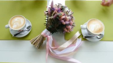 Kapatın. Üst Manzara. Erkek ve kadın elleri kahve içiyor. Ortasında yaz çiçekleri olan bir buket. Yüksek çözünürlüklü çekim