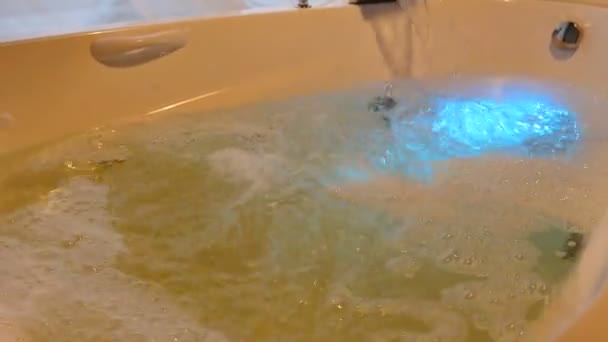 Vízzel és habbal teli fürdő. Vízáramlás a fürdőbe habbal. Jacuzzi belső fényforrással. Közelről. Hd-ben lőtték le — Stock videók