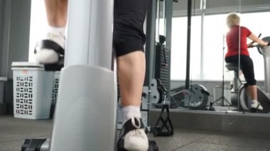 70 'lerinde mutlu aktif bir kadın. Yaşlı kadın spor salonunda kardiyo eğitimi alıyor. Sağlıklı bunaklık konsepti. Spor salonunda bisiklete binen yaşlı bir kadın. 4K 'da çekim.