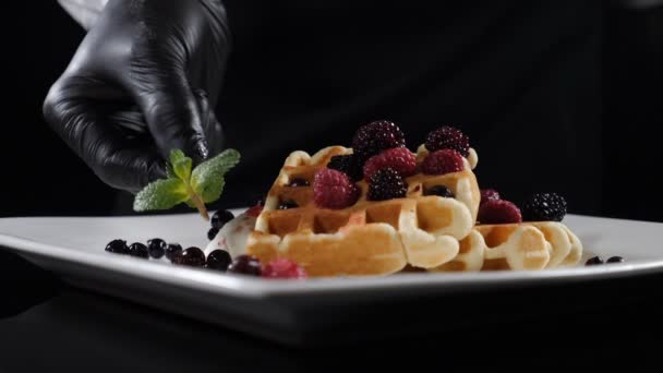 El chef pone hojas de menta en el plato con gofres de sudor decorados con bayas. Vídeo de comida en cámara lenta. Delicioso postre en plato blanco. Chef plato de cortesía. Pastelería en panadería. Full hd — Vídeos de Stock