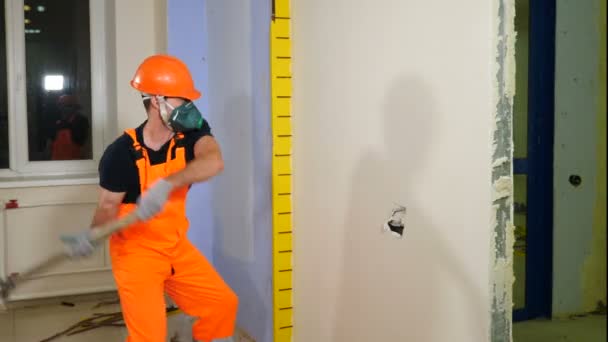 Trabalho de demolição e conceito de rearranjo. Trabalhador masculino em uniforme e respirador destruindo a parede interna com marreta. remodelação no novo apartamento, derrubando a parede interior. 4 k imagens — Vídeo de Stock