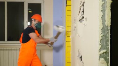 Yıkım işi ve yeniden düzenleme konsepti. Üniformalı ve solunum cihazlı bir erkek balyozla iç duvarı yok ediyor. Yeni dairede yeniden yapılanma, iç duvarı yıkma. 4k görüntü